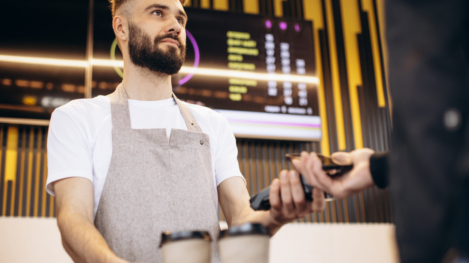 Male barista holding terminal while customer paying with card