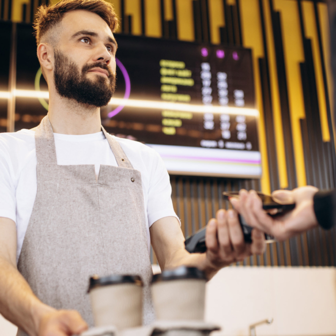 Male barista holding terminal while customer paying with card