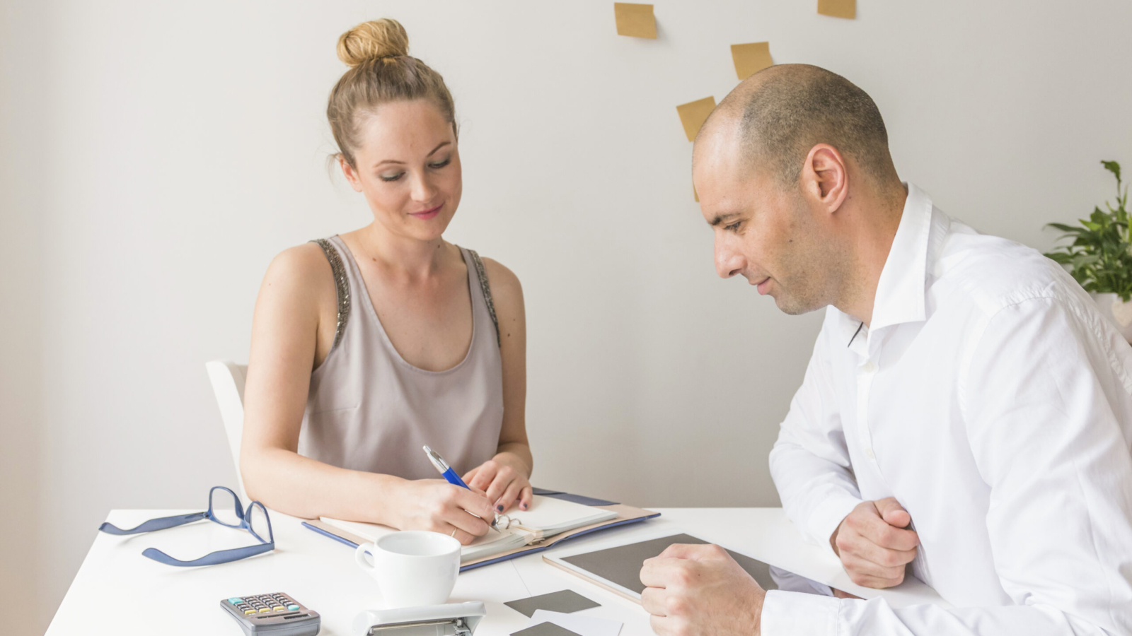 businessman-looking-businesswoman-writing-diary-workplace